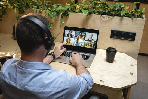 Männlicher Unternehmer bei einem Videogespräch mit Kollegen über einen Laptop, während er am Schreibtisch in einem kreativen Büro sitzt - VPIF02763