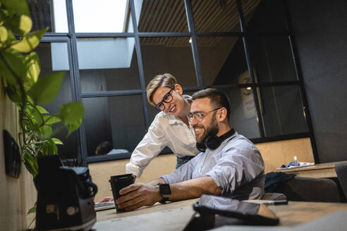 Lächelnde männliche und weibliche Unternehmer, die auf einen Laptop schauen, während sie im Büro eine Strategie planen - VPIF02766