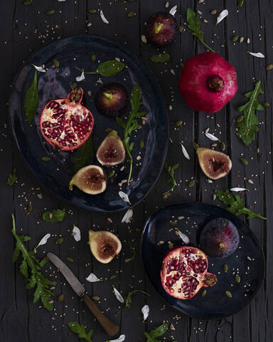 Top view of fresh cut figs and pomegranates placed on plates near arugula and knife on lumber table stock photo