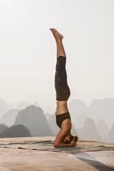 Beautiful woman practising yoga above the kast mountains of Yangshuo - CAVF88260