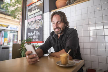 Man enjoying in a coffee shop while looking at the mobile phone - CAVF88265