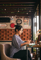 Woman working over coffee, checking her cell phone - CAVF88267