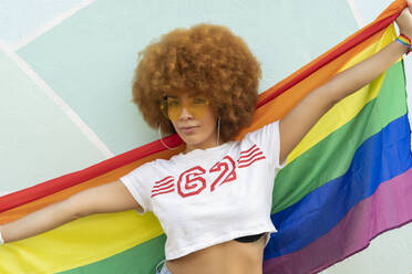 Frau mit Afro-Haar auf blauer Wand, die die Homosexuell Stolz Flagge zeigt - CAVF88287