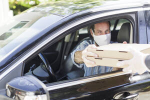 Man in fabric mask receives pizza through curbside pickup - CAVF88304