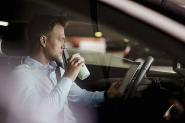 Geschäftsmann mit Kaffee, der im Auto auf einem digitalen Tablet online liest - DIGF12800