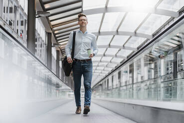 Businessman with coffee cup looking away while walking in city - DIGF12821