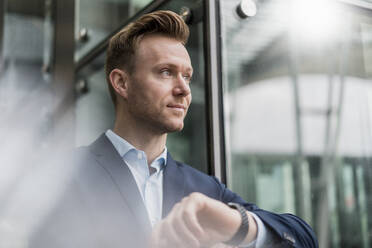 Confident entrepreneur wearing wristwatch while looking away in city - DIGF12836