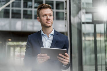 Selbstbewusster Geschäftsmann mit digitalem Tablet, der in der Stadt wegschaut - DIGF12837