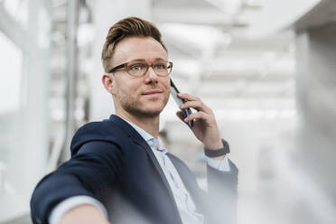 Businessman wearing eyeglasses talking on phone while sitting in city - DIGF12846