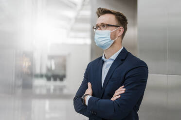 Businessman with arms crossed wearing mask in city - DIGF12850