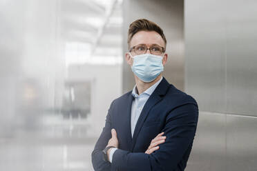 Businessman with arms crossed wearing face mask in city - DIGF12851