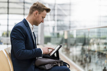 Businessman with bag using digital tablet while sitting in city - DIGF12855