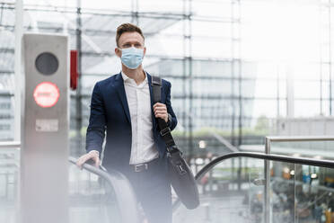 Businessman with bag wearing face mask in city - DIGF12859
