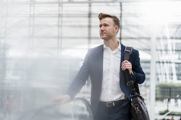 Businessman with bag walking by escalator in city - DIGF12860