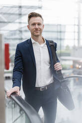 Confident businessman with bag walking by escalator in city - DIGF12861