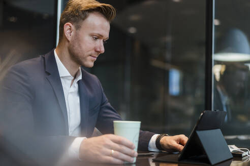 Geschäftsmann mit Kaffee und digitalem Tablet am Tisch in einem Café - DIGF12863