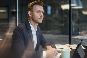 Businessman with coffee and digital tablet at table in cafe - DIGF12865