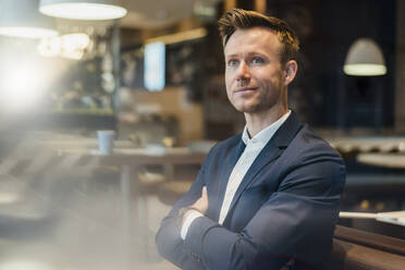 Businessman with arms crossed sitting in cafe - DIGF12869