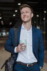 Lächelnder Geschäftsmann trinkt Kaffee beim Spaziergang in der Stadt - DIGF12872