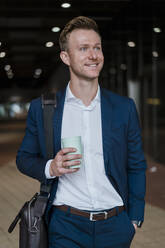 Lächelnder Unternehmer trinkt Kaffee beim Spaziergang in der Stadt - DIGF12873