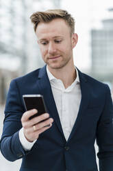 Confident businessman texting through mobile phone in city - DIGF12893