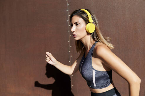 Woman listening to music while running against wall - KIJF03219
