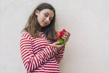 Mädchen hält Hibiskusblüte und steht an der Wand - DLTSF01075