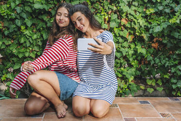 Smiling sisters taking selfie through smart phone in backyard - DLTSF01080