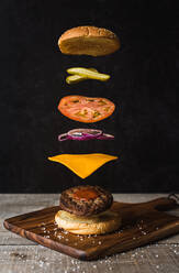 Burger mit schwimmenden getrennten Zutaten auf schwarzem Hintergrund. - CAVF88328