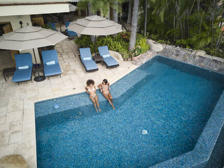 Female friends relaxing in swimming pool at villa - ABAF02303