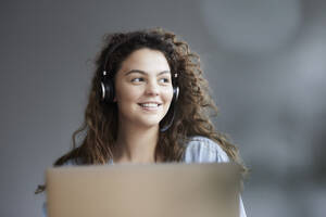 Lächelnde junge Frau trägt ein Headset, während sie zu Hause einen Laptop benutzt - FMKF06240