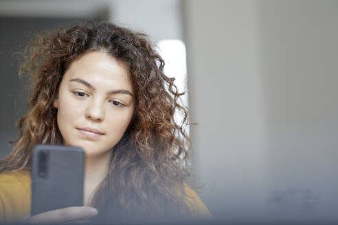 Schöne junge Frau, die zu Hause ein Mobiltelefon benutzt - FMKF06244