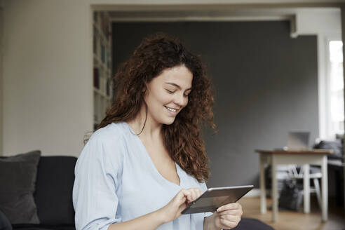 Lächelnde Frau, die zu Hause ein digitales Tablet benutzt - FMKF06249