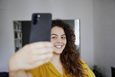Glückliche junge schöne Frau nimmt Selfie zu Hause - FMKF06256