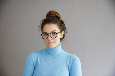 Selbstbewusste junge Frau mit Brille vor grauer Wand - FMKF06270