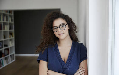 Young woman with arms crossed leaning on wall at home - FMKF06278