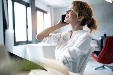 Smiling woman talking on phone at home office - JSRF01013