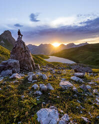 Wanderer sitzt bei Sonnenuntergang auf einem Felsen am Rappensee, Bayern, Deutschland - MALF00070