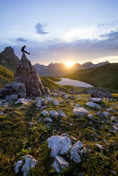 Hiker sitting on rock during sunset at Lake Rappensee, Bavaria, Germany - MALF00071