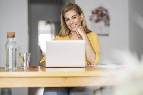 Lächelnde reife Frau benutzt Laptop zu Hause - JSMF01682