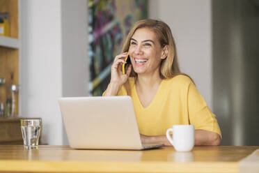 Smiling woman talking on mobile phone while sitting at table - JSMF01686