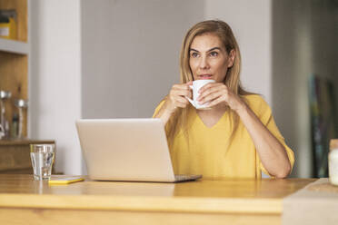Nachdenkliche reife Frau trinkt Kaffee, während sie am Tisch sitzt - JSMF01688