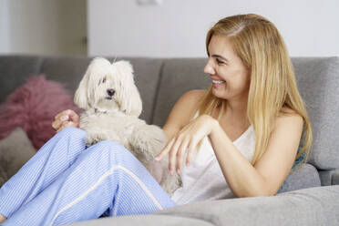 Glückliche reife Frau mit Hund entspannt auf dem Sofa zu Hause - JSMF01690