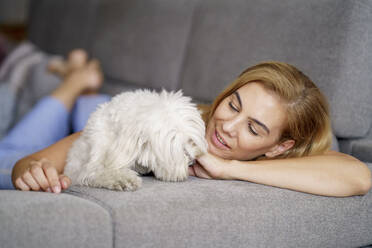 Frau entspannt sich mit Hund auf Sofa zu Hause - JSMF01693