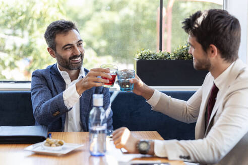 Geschäftsleute stoßen mit Getränken an, während sie am Tisch im Café sitzen - JSRF01019