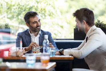 Smiling businessman discussing with coworker at cafe - JSRF01026