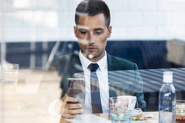 Businessman using smart phone in cafe seen through glass window - JSRF01028