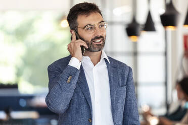 Businessman talking on mobile phone while standing at cafe - JSRF01031