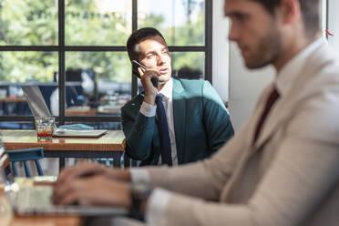 Businessman looking away while talking on mobile phone in restaurant - JSRF01033