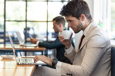 Junger Geschäftsmann trinkt Kaffee und benutzt einen Laptop in einem Café - JSRF01034